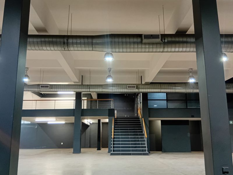 Spacious open-plan retail or commercial area featuring high ceilings, exposed industrial ductwork, a mezzanine level, and a central staircase.