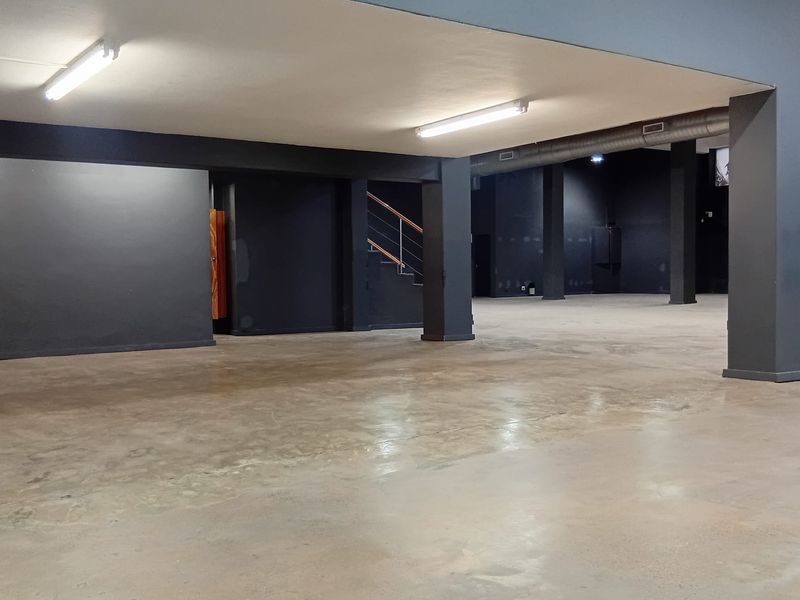 A spacious, open-plan retail area featuring polished concrete floors, exposed industrial ducting, and modern dark-toned walls with integrated staircase access.