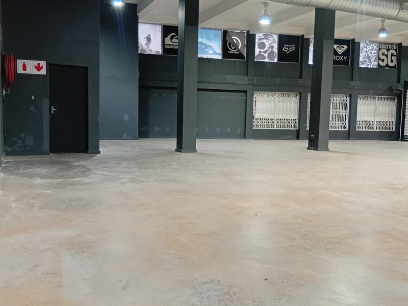Spacious open-plan retail area featuring industrial exposed ducting, structural columns, and secure access points, suitable for a variety of commercial uses.