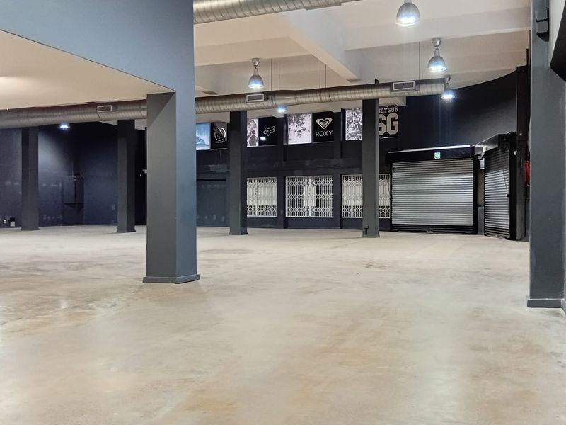 Spacious open-plan retail area featuring industrial-style exposed ducting, concrete flooring, structural columns, and secure roller shutter access.
