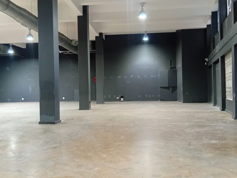 Spacious open-plan retail area featuring high ceilings, exposed industrial ducting, concrete flooring, and structural columns, offering a versatile blank canvas for commercial use.
