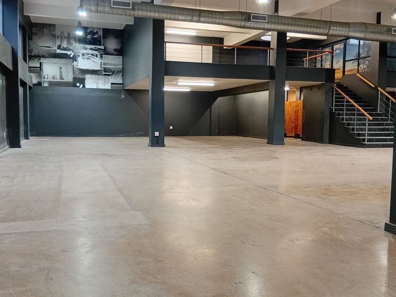Spacious open-plan retail or commercial area featuring polished concrete floors, exposed industrial ductwork, a mezzanine level, and a modern staircase.