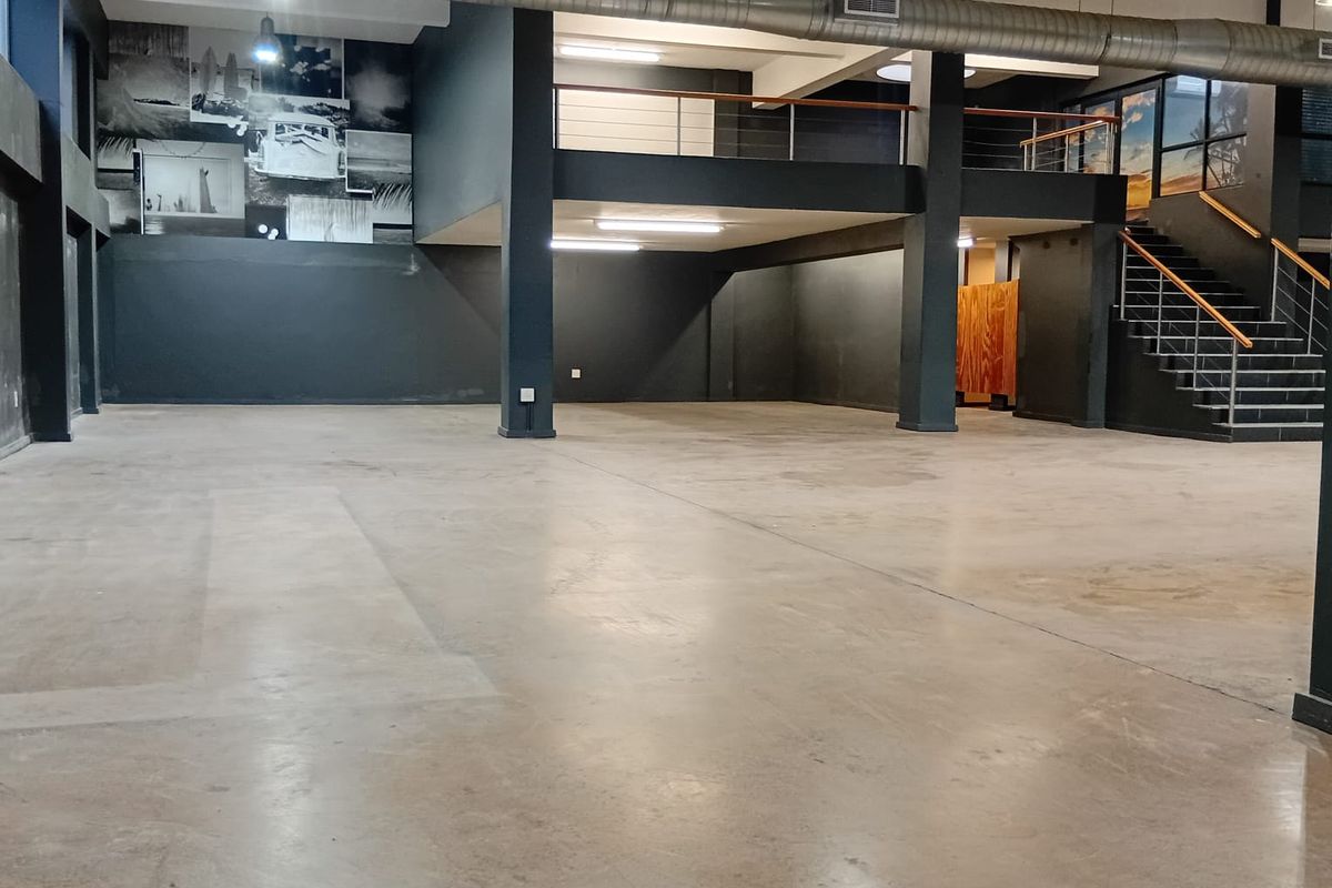 Spacious open-plan retail or commercial area featuring polished concrete floors, exposed industrial ductwork, a mezzanine level, and a modern staircase.