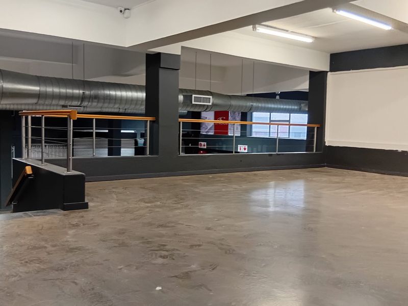 An open-plan commercial space featuring polished concrete floors, exposed industrial ducting, and a mezzanine level with a modern railing.