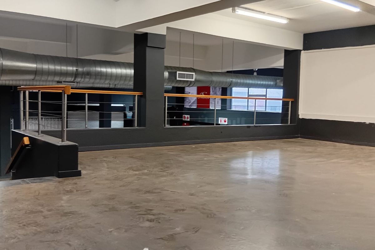 An open-plan commercial space featuring polished concrete floors, exposed industrial ducting, and a mezzanine level with a modern railing.