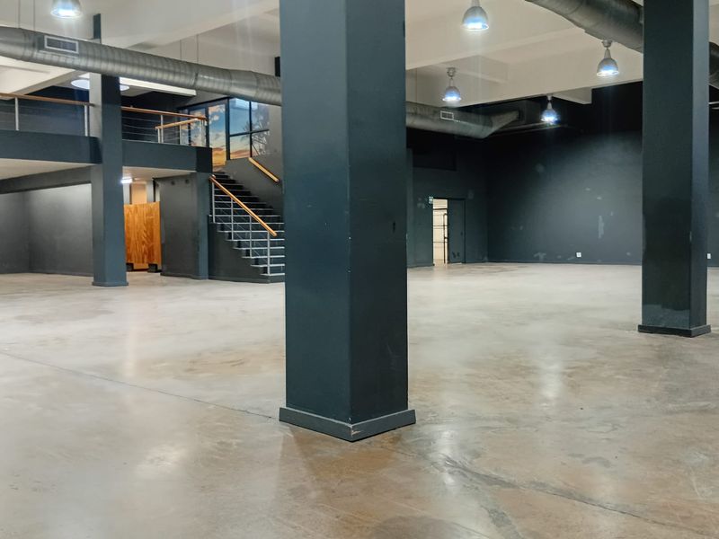 Spacious open-plan retail area featuring industrial-style exposed ducting, polished concrete floors, structural columns, and a mezzanine level with a staircase.