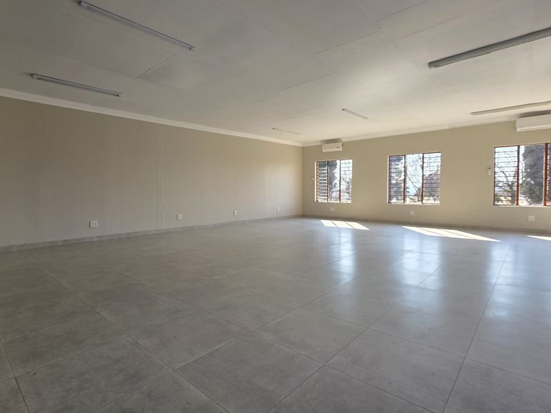 A spacious, vacant office area featuring neutral tiled flooring, multiple windows with security bars, and integrated split-system air conditioning units.