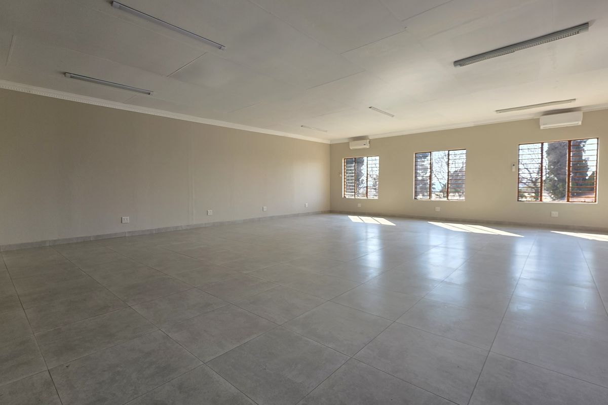 A spacious, vacant office area featuring neutral tiled flooring, multiple windows with security bars, and integrated split-system air conditioning units.