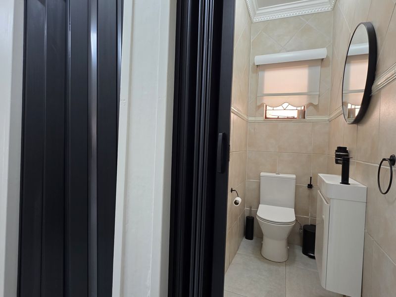 A compact, well-maintained bathroom featuring tiled walls, a modern vanity basin, and a toilet, accessed through a folding door.