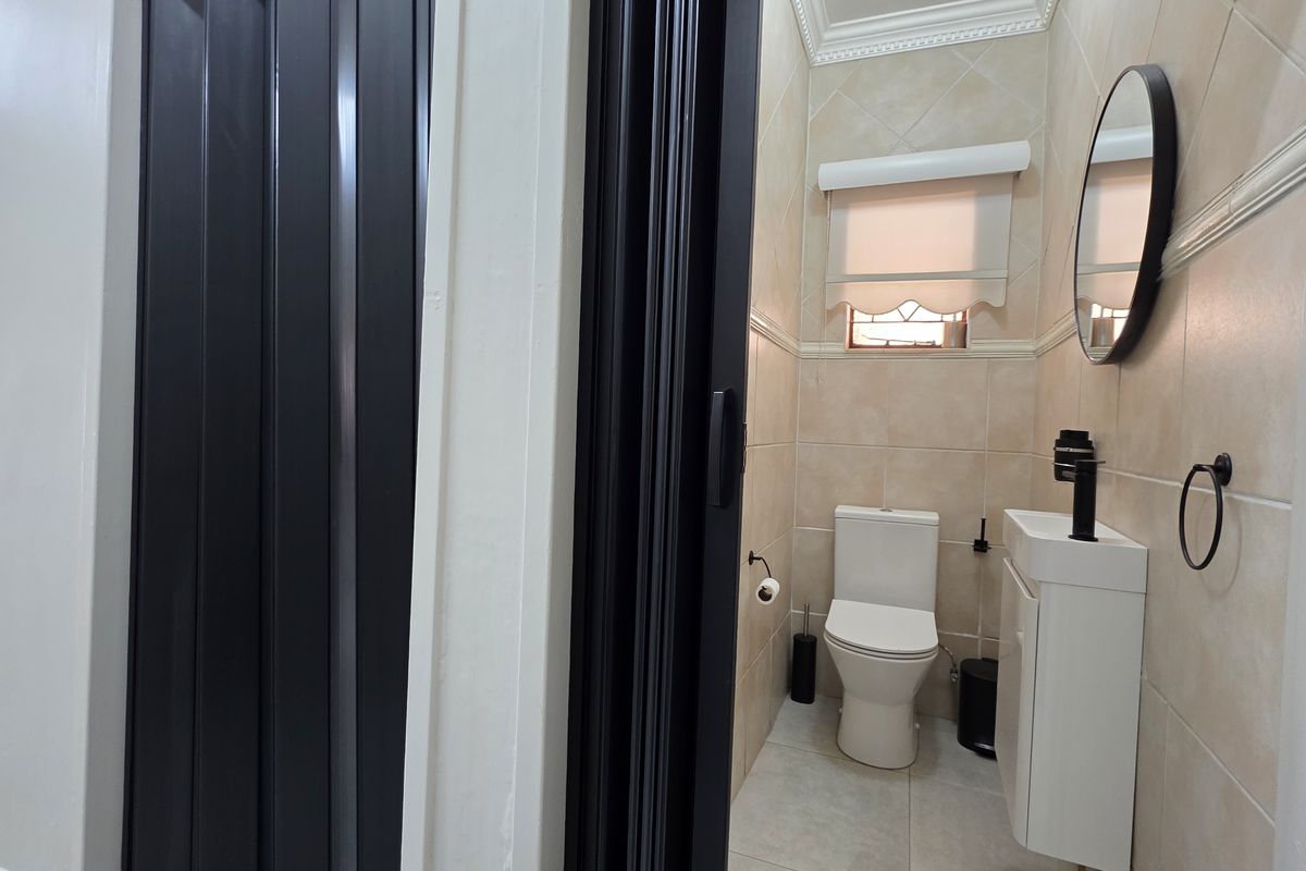 A compact, well-maintained bathroom featuring tiled walls, a modern vanity basin, and a toilet, accessed through a folding door.