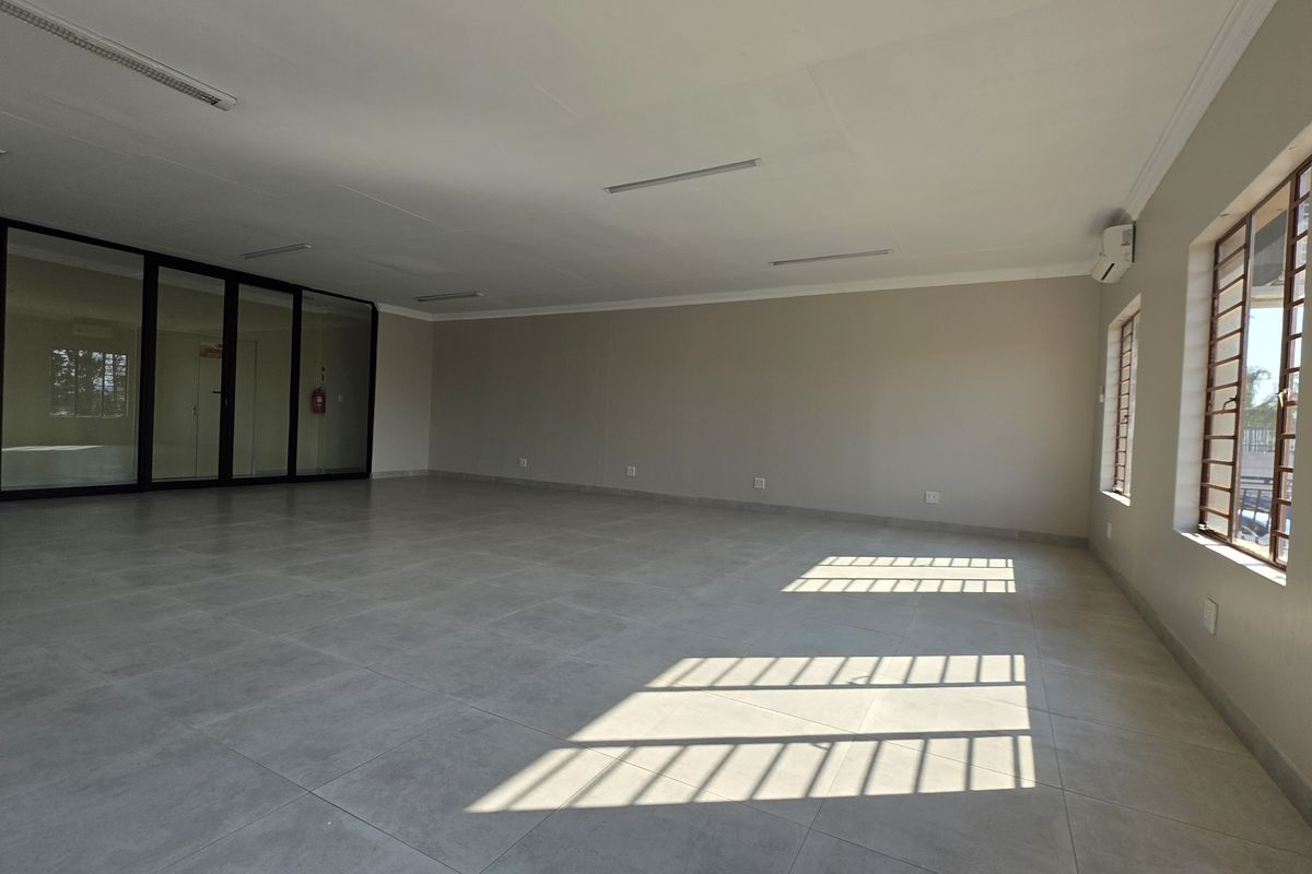 A spacious, empty office area featuring large tiled floors, neutral walls, glass partitioning, and security bars on the windows, providing a clean professional workspace.
