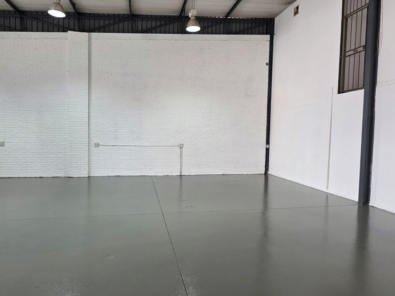 Spacious industrial warehouse unit featuring high ceilings with exposed trusses, durable epoxy flooring, and clean painted brick walls, suitable for various commercial uses.