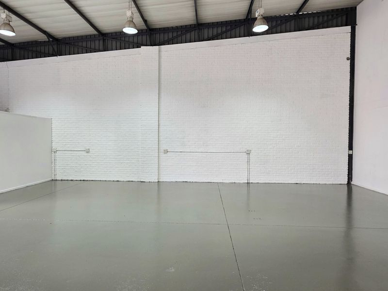 Spacious industrial warehouse unit featuring high ceilings with exposed trusses, durable epoxy flooring, and clean white painted brick walls.