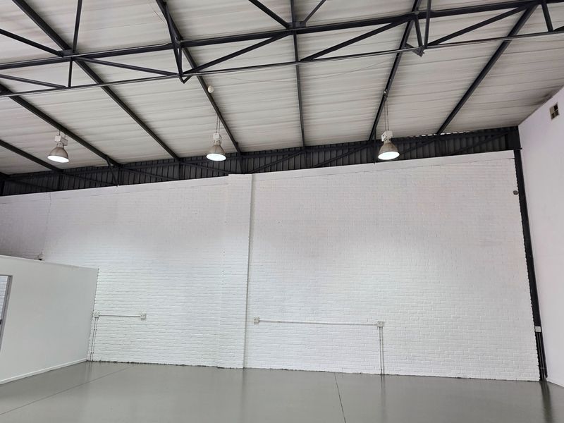 Spacious industrial warehouse unit featuring high ceilings with exposed steel trusses, durable epoxy flooring, and clean white-painted brick walls.