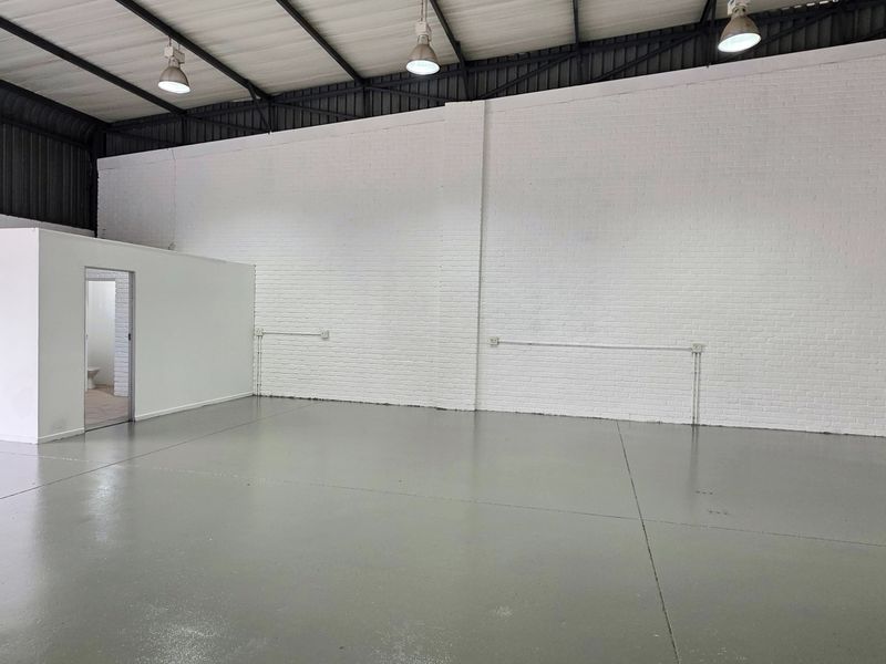 Spacious industrial warehouse unit featuring high ceilings with exposed trusses, durable epoxy flooring, painted brick walls, and a dedicated internal partitioned room.