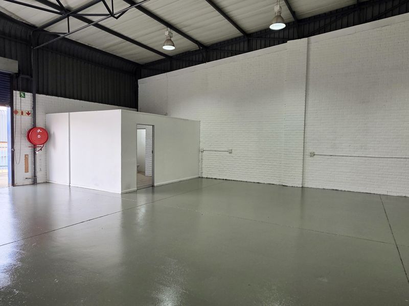 Spacious industrial warehouse unit featuring high ceilings with exposed trusses, durable epoxy flooring, and a dedicated internal partitioned office space.