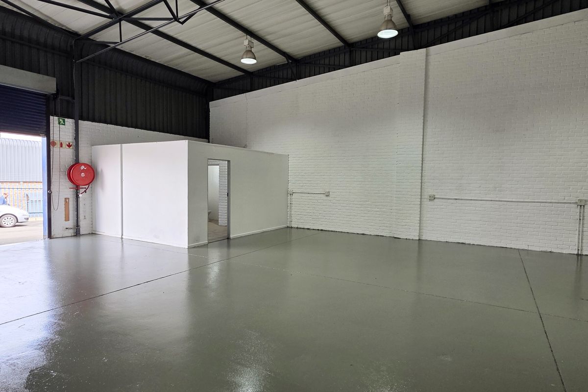 Spacious industrial warehouse unit featuring high ceilings with exposed trusses, durable epoxy flooring, and a dedicated internal partitioned office space.