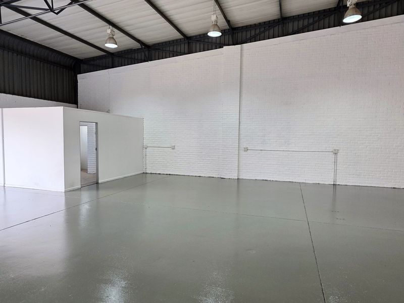 Spacious industrial warehouse unit featuring polished epoxy flooring, high exposed ceilings with pendant lighting, and a dedicated internal partitioned office space.