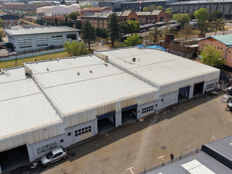 Aerial view of an industrial warehouse complex featuring corrugated metal roofing, multiple roller shutter access doors, and a paved yard area.