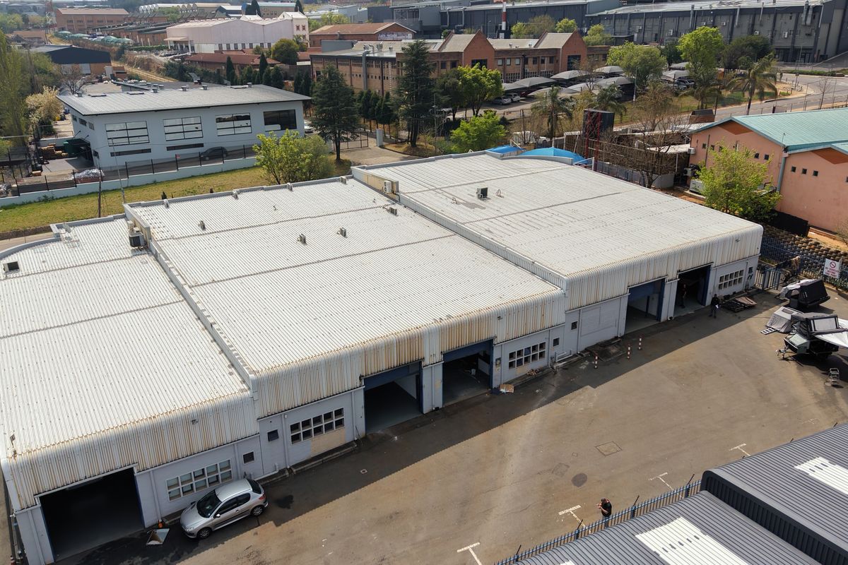 Aerial view of an industrial warehouse complex featuring corrugated metal roofing, multiple roller shutter access doors, and a paved yard area.