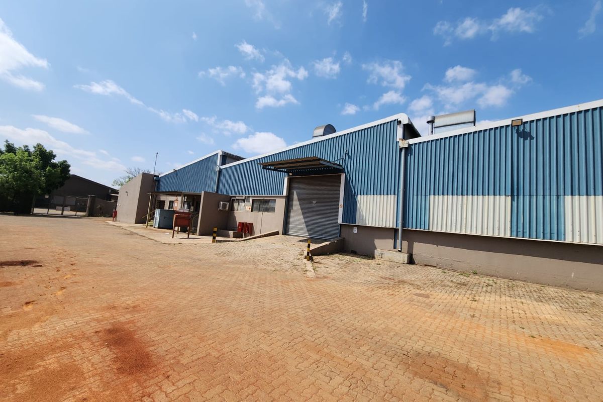 Industrial warehouse exterior featuring corrugated metal cladding, a roller shutter door, and a paved yard area suitable for loading and logistics.