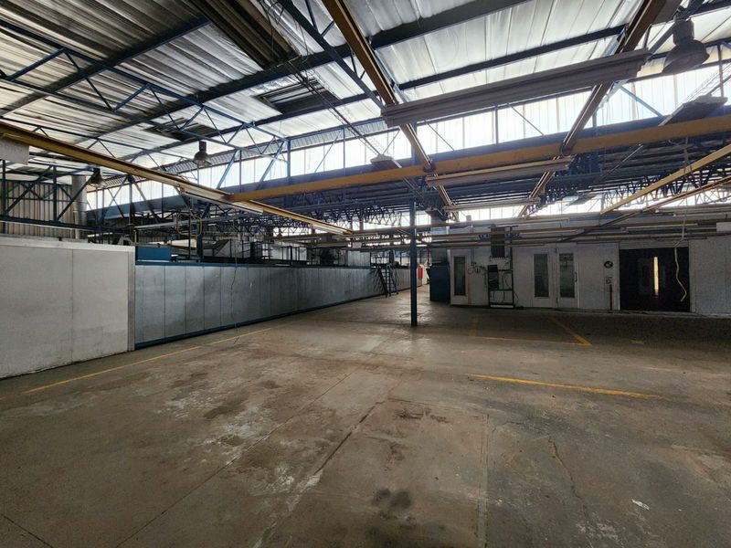 Spacious industrial warehouse area featuring exposed steel roof trusses, overhead crane rails, and durable concrete flooring, suitable for manufacturing or storage operations.