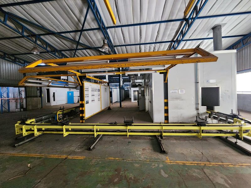 Industrial warehouse space featuring an integrated conveyor system, overhead gantry, and exposed steel roof trusses with durable concrete flooring.