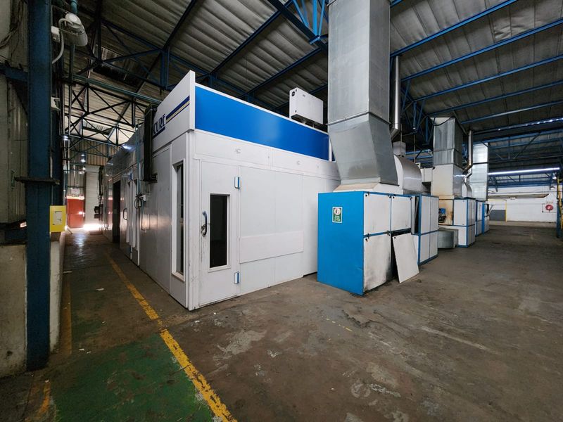 Industrial warehouse space featuring a large built-in spray booth with integrated ventilation ducting and exposed steel roof structure.