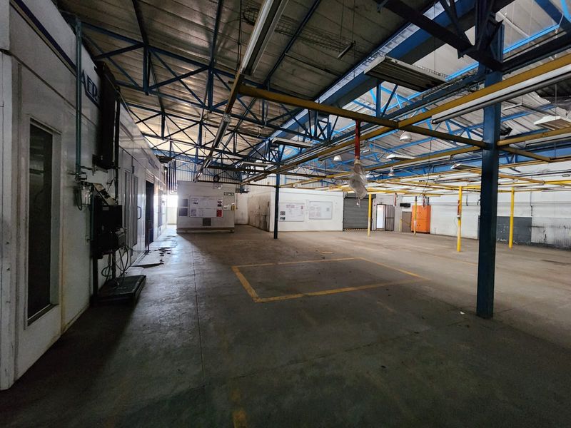 Spacious industrial warehouse area featuring exposed steel roof trusses, concrete flooring, and an integrated spray booth facility.