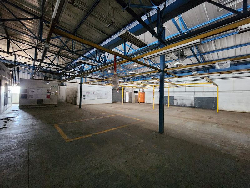 Spacious industrial utility area featuring exposed steel roof trusses, concrete flooring, and an overhead lighting grid, suitable for warehouse or workshop operations.