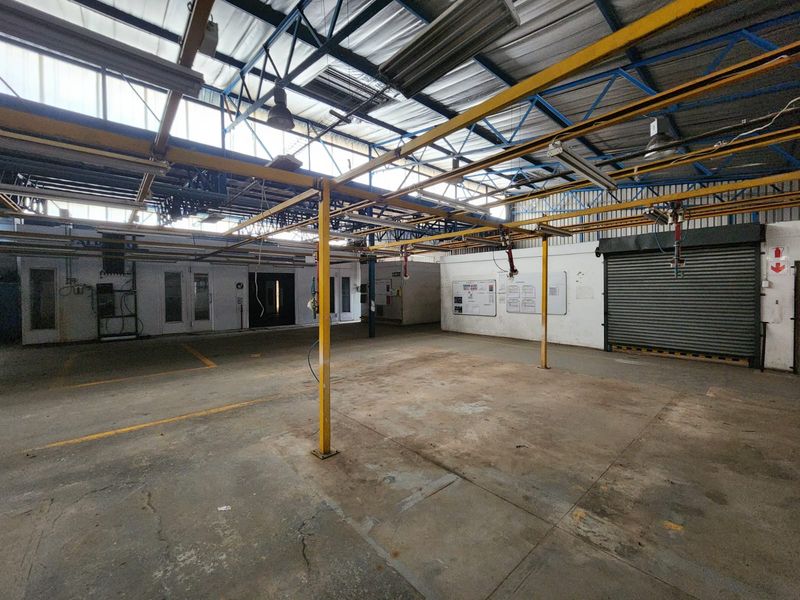 Spacious industrial utility area featuring high ceilings with exposed steel trusses, an overhead gantry system, concrete flooring, and a secure roller shutter door.