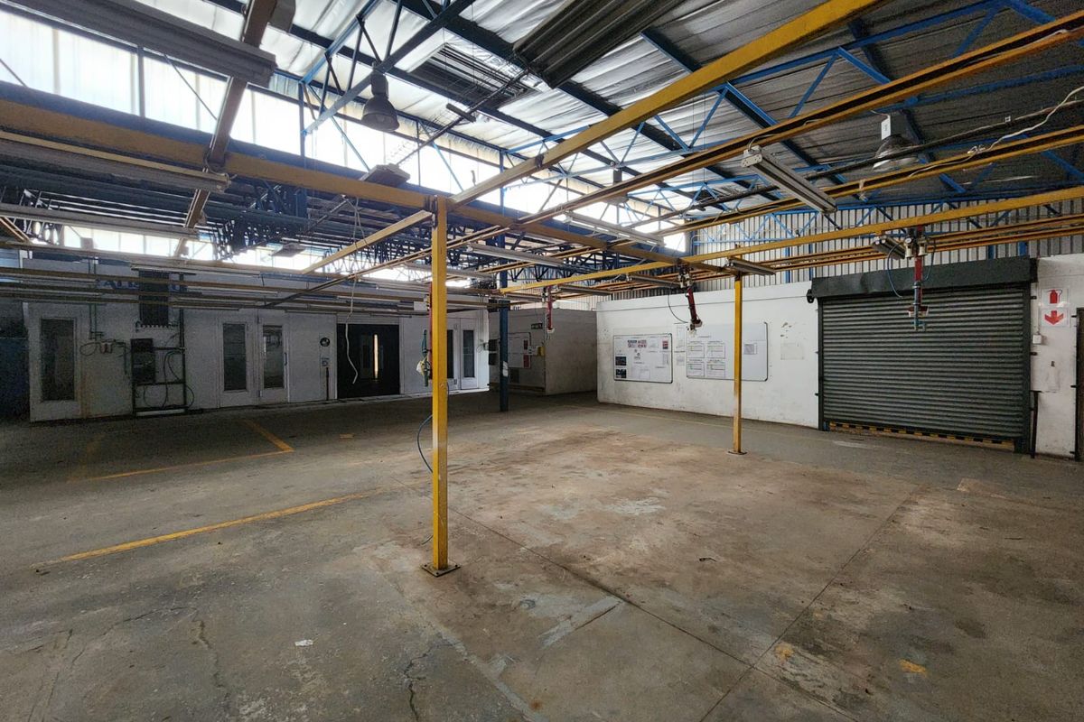 Spacious industrial utility area featuring high ceilings with exposed steel trusses, an overhead gantry system, concrete flooring, and a secure roller shutter door.
