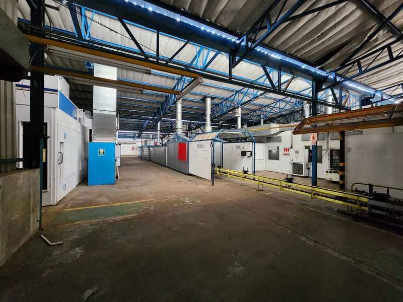 Spacious industrial warehouse facility featuring exposed steel roof trusses, integrated ventilation systems, concrete flooring, and built-in industrial processing equipment.