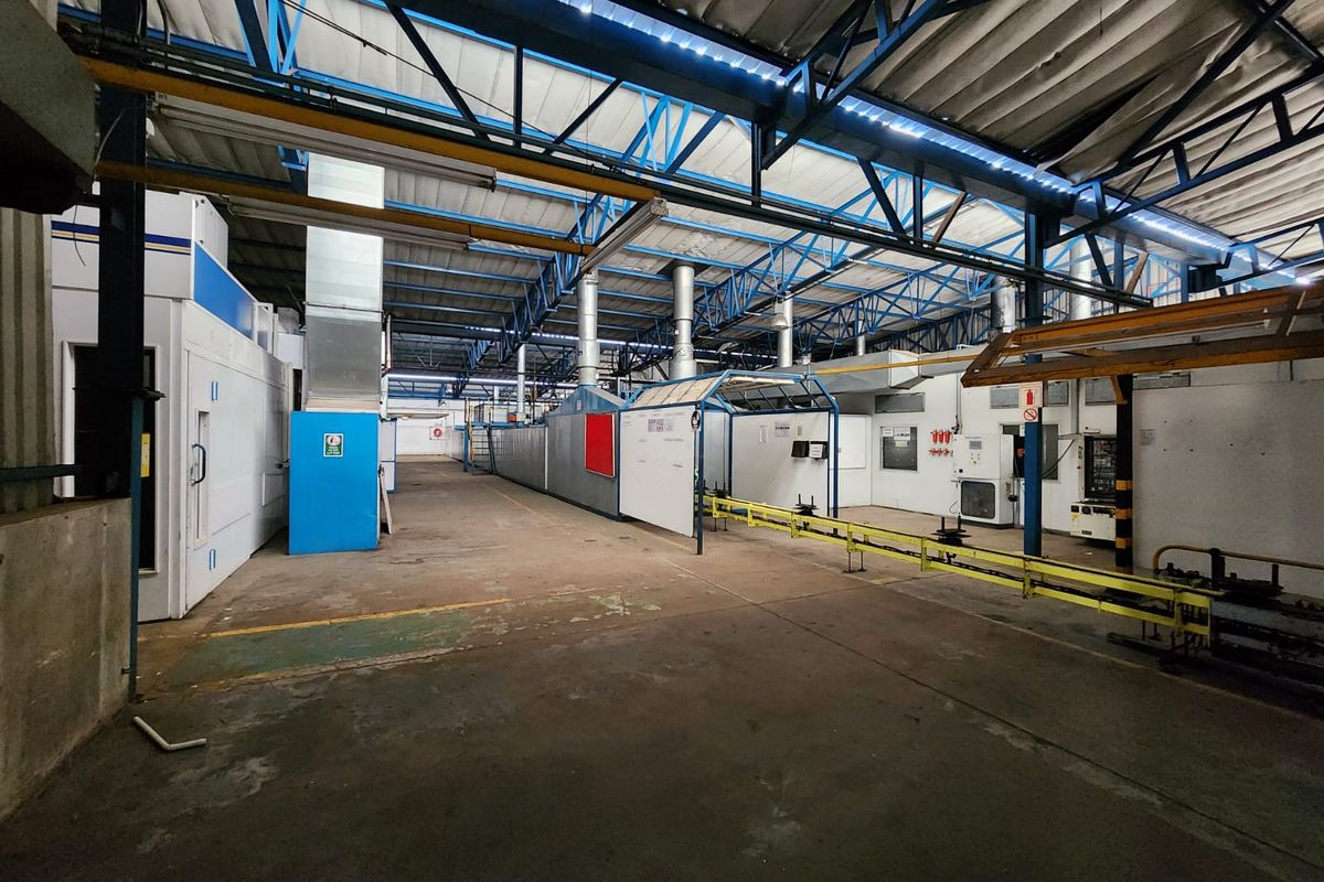 Spacious industrial warehouse facility featuring exposed steel roof trusses, integrated ventilation systems, concrete flooring, and built-in industrial processing equipment.