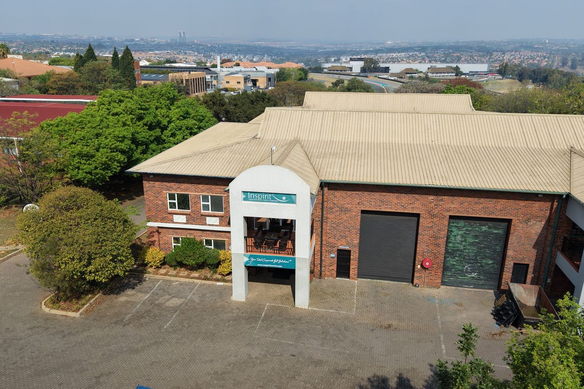 Aerial view of an industrial property featuring a brick facade, metal roofing, roller shutter doors, and a paved parking area.