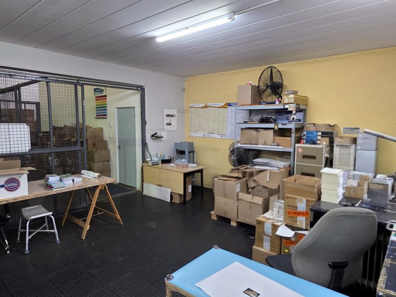 Industrial utility or workshop space featuring durable rubber flooring, a secure metal storage cage, and overhead fluorescent lighting.