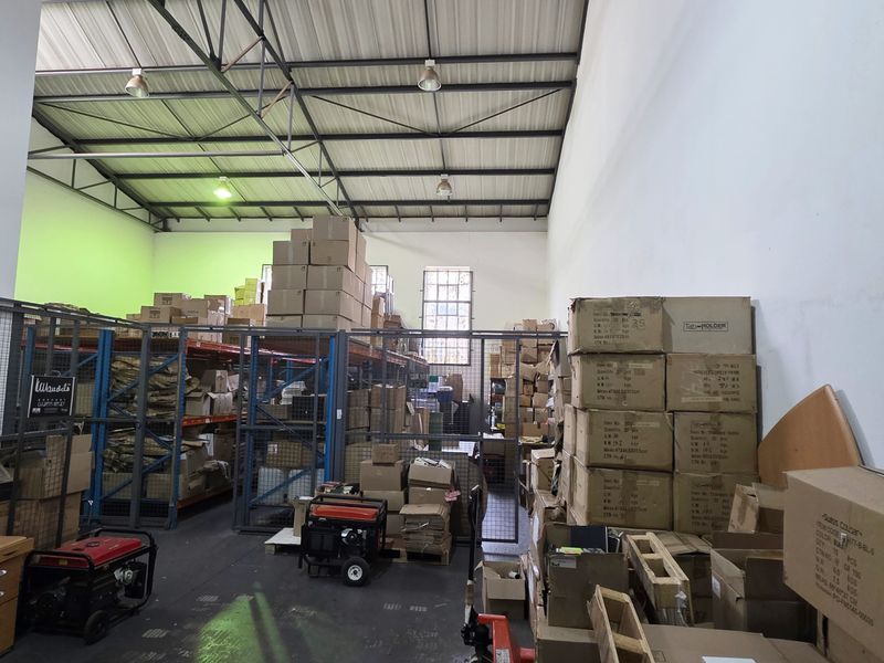 Industrial warehouse space featuring high ceilings with exposed steel trusses, concrete flooring, and integrated metal storage racking with security mesh partitioning.