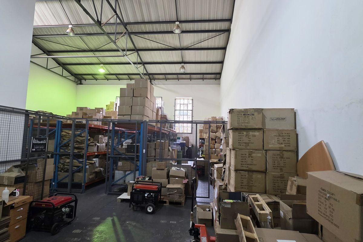 Industrial warehouse space featuring high ceilings with exposed steel trusses, concrete flooring, and integrated metal storage racking with security mesh partitioning.