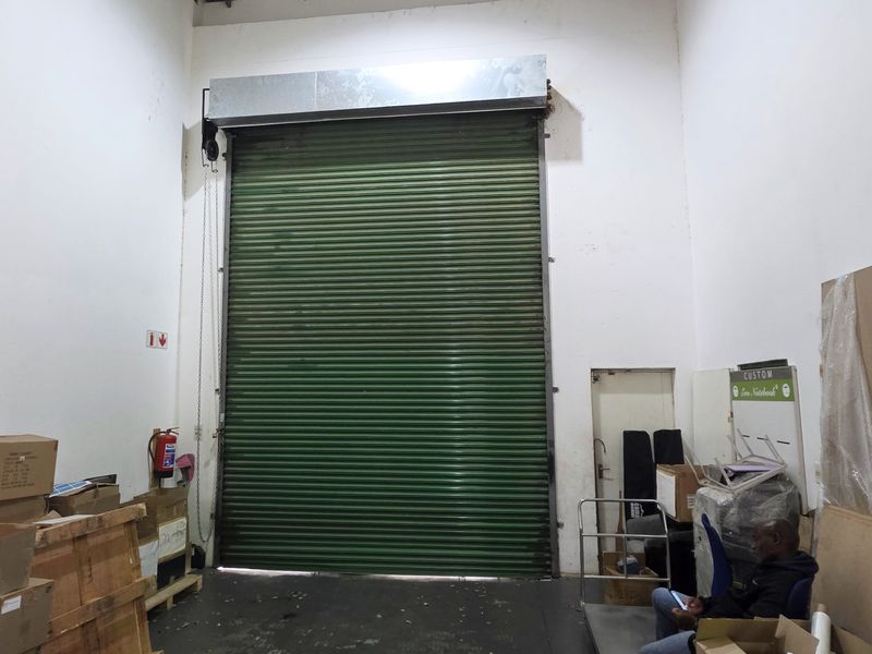 Industrial utility space featuring a large green roller shutter door and high ceilings, suitable for storage or logistics operations.