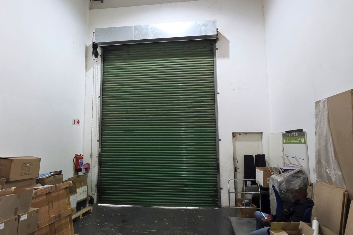 Industrial utility space featuring a large green roller shutter door and high ceilings, suitable for storage or logistics operations.