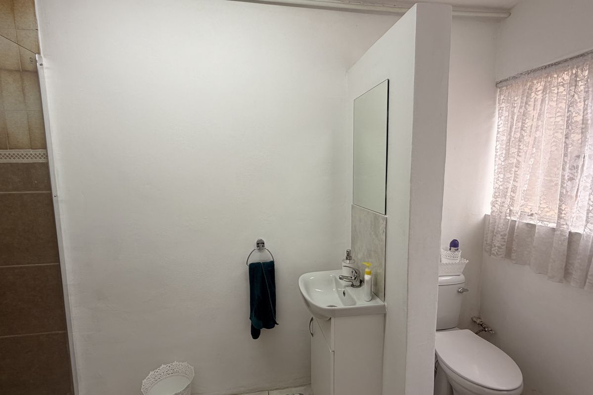 A functional bathroom featuring a shower enclosure, wall-mounted basin with vanity storage, and a standard toilet, finished with neutral wall paint and tiled shower area.