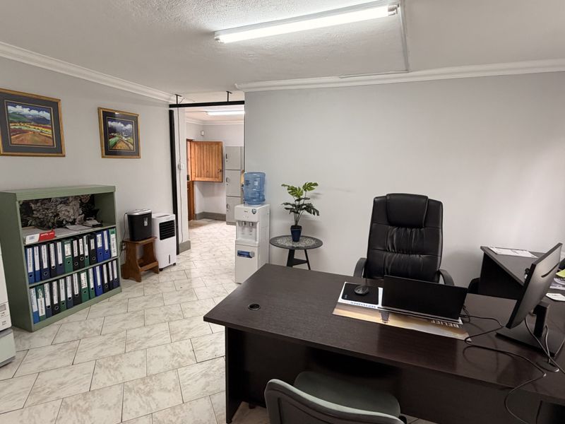 A functional office space featuring tiled flooring, neutral walls, and overhead fluorescent lighting, providing a practical work environment.