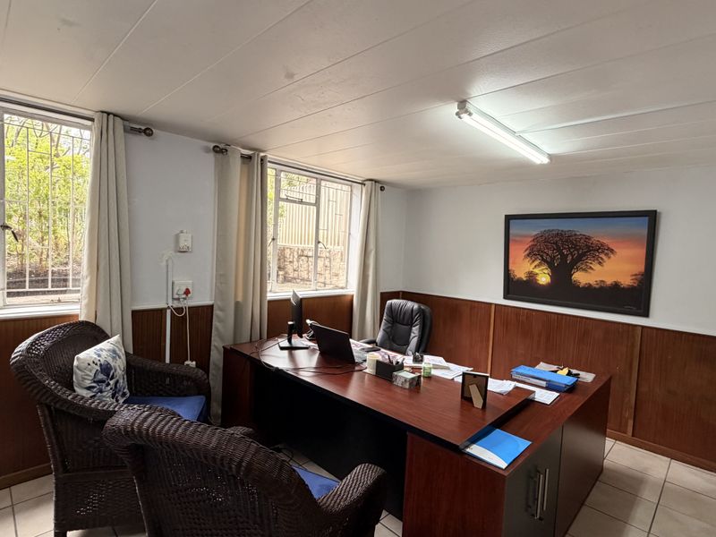 A functional office space featuring wood paneling, tiled flooring, and large windows with security bars, providing natural light and a professional work environment.