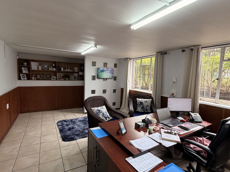 A functional office space featuring tiled flooring, built-in shelving, wood wall paneling, and large windows providing natural light.