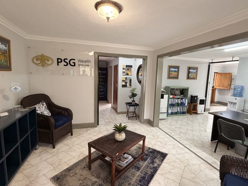 A professional office reception area featuring tiled flooring, crown molding, and clear signage, leading into an adjacent workspace.