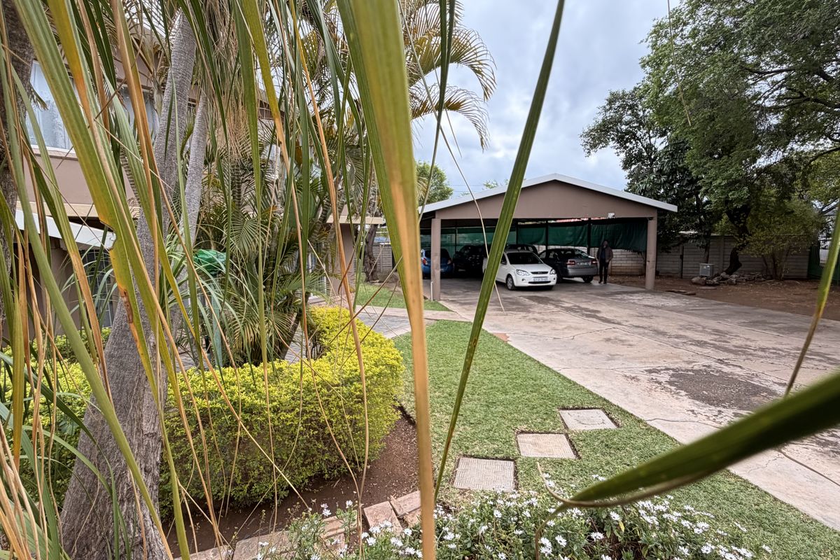 Exterior view of the property featuring a covered carport, concrete driveway, and established garden area.