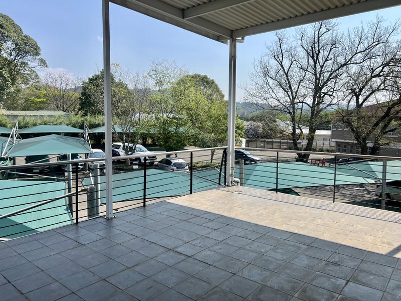 A spacious covered balcony featuring tiled flooring and metal railings, offering an elevated view over the property's parking area.
