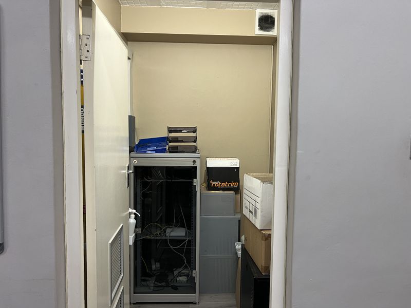 A small utility or server room featuring a built-in server rack and wall-mounted ventilation grille.