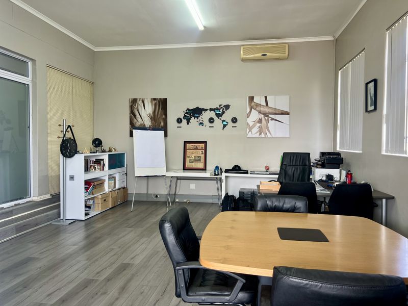 A functional office space featuring laminate flooring, vertical blinds, and a wall-mounted air conditioning unit, suitable for professional use.