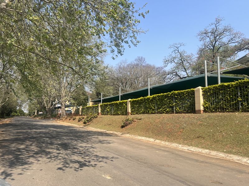 Street view of the office property perimeter, featuring secure metal fencing, brick pillars, and overhead shade netting structures along the roadside.